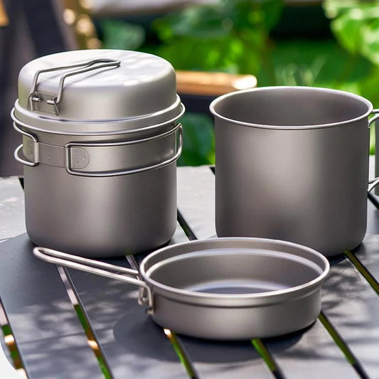 Set of camping cookware including pots and a pan on a wooden surface with a natural background.